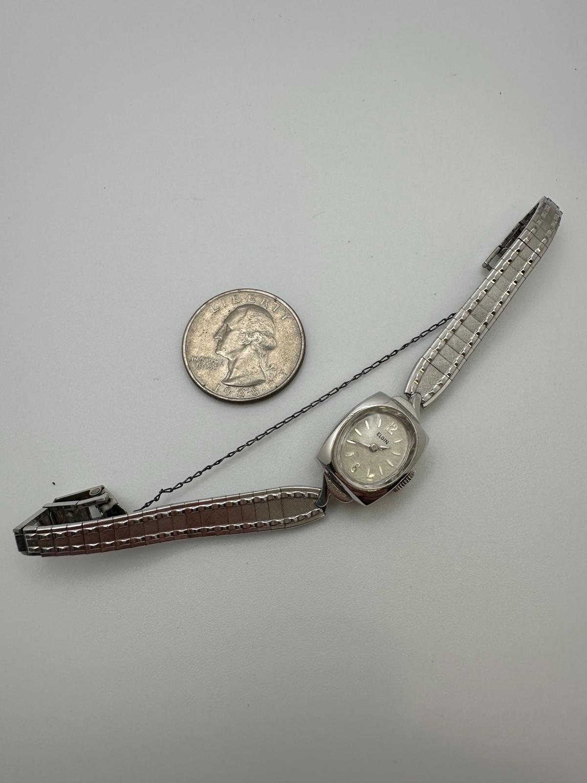 Small wristwatch with brown strap next to a quarter on a gray background